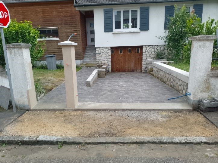 Construction d'une entrée de garage résidentielle avec des piliers et une allée pavée.