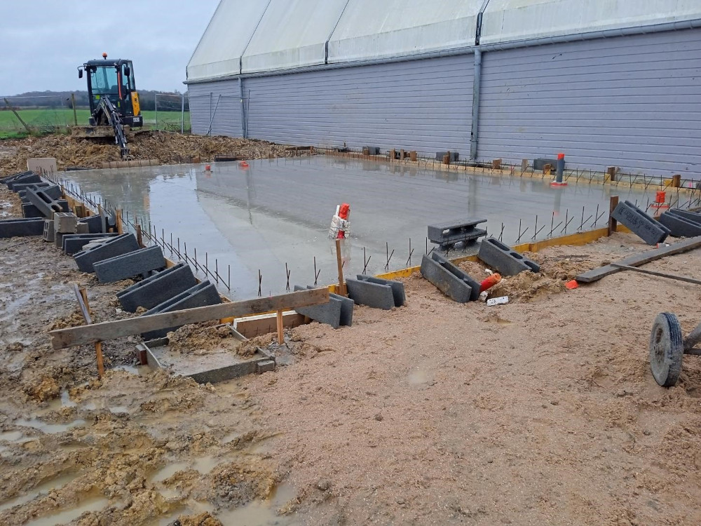 Pose d'une dalle de béton pour un bâtiment agricole en construction.